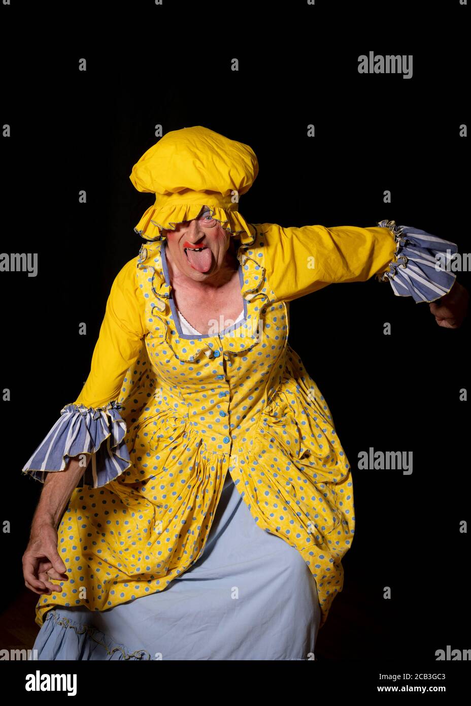 An ugly sister in a bright yellow dress and matching hat during an amateur dramatic society production of Cinderella. Stock Photo