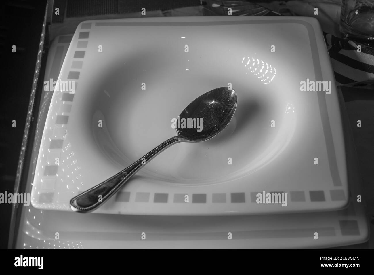 A lone soup bowl in black & white with contrast and single spoon providing contrast. Good mood and lighting Stock Photo