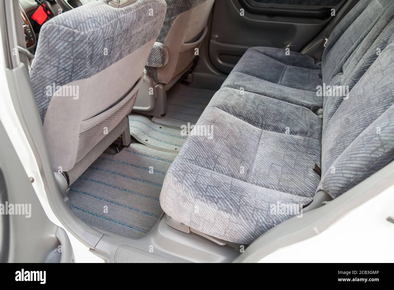The open back door of a white sedan is a row of passenger seats covered in dark gray fabric after dry cleaning; pre-sale preparation of the car. Stock Photo