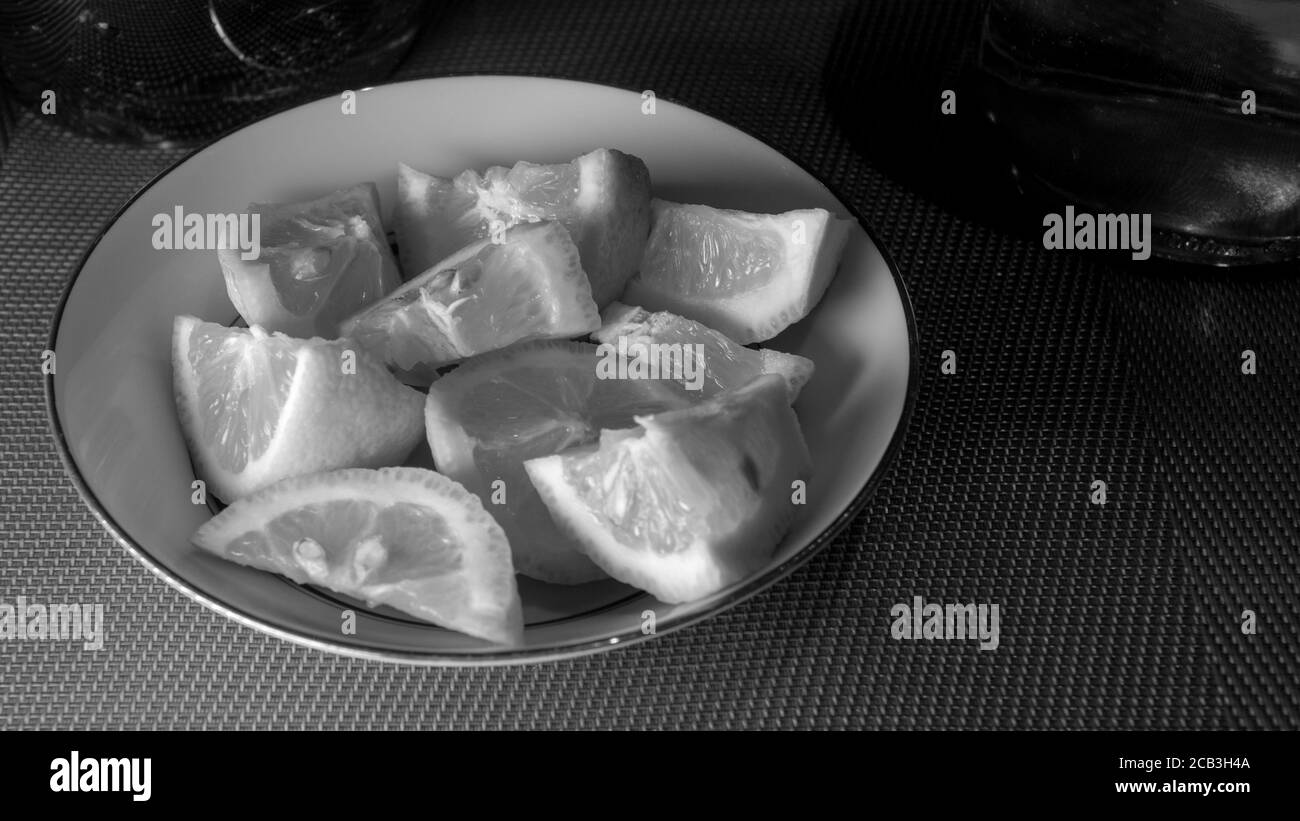 Sliced lemon stacked in a bowl in black and white ready to be served as an accompaniment for a meal. There is moody lighting with contrast. Stock Photo