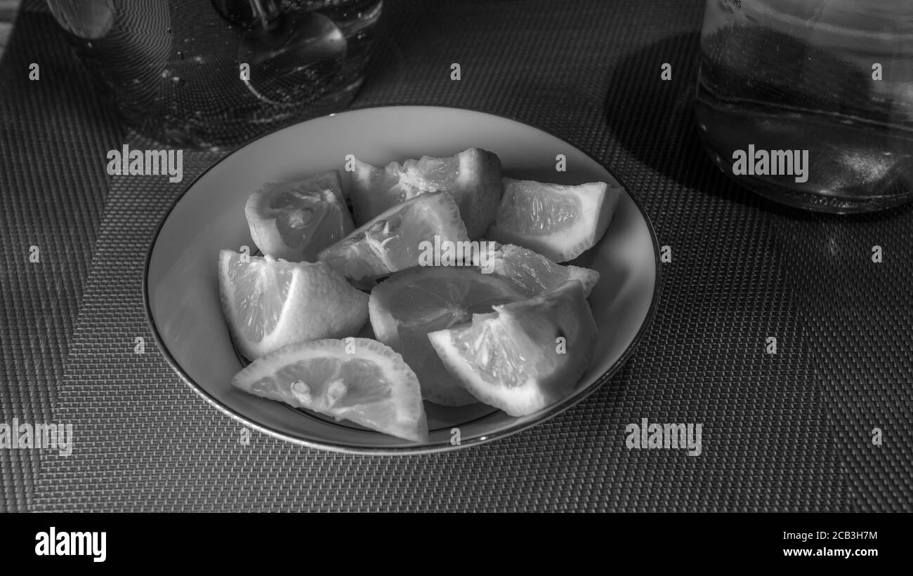 Sliced lemon stacked in a bowl in black and white ready to be served as an accompaniment for a meal. There is moody lighting with contrast. Stock Photo