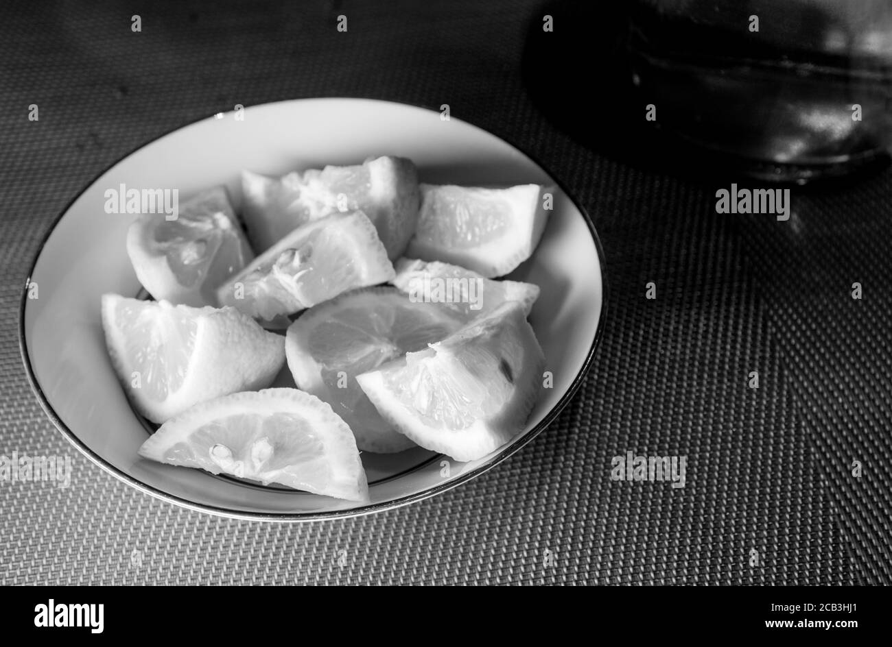 Sliced lemon stacked in a bowl in black and white ready to be served as an accompaniment for a meal. There is moody lighting with contrast. Stock Photo