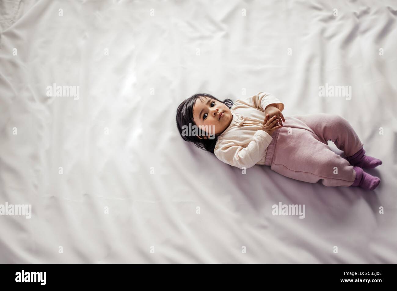 adorable lovely Afro American baby girl looking at camera while lying on comfortable bed, top view photo. love concept, copy space Stock Photo
