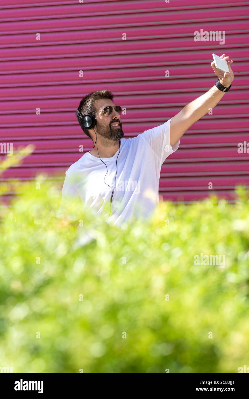 Bearded guy with sunglasses taking a selfie against pink wall Stock Photo