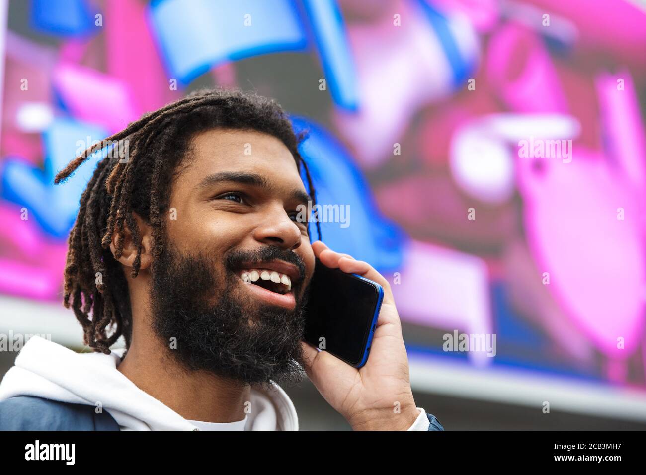 Image closeup of african american joyful man smiling and talking on mobile phone at city street Stock Photo