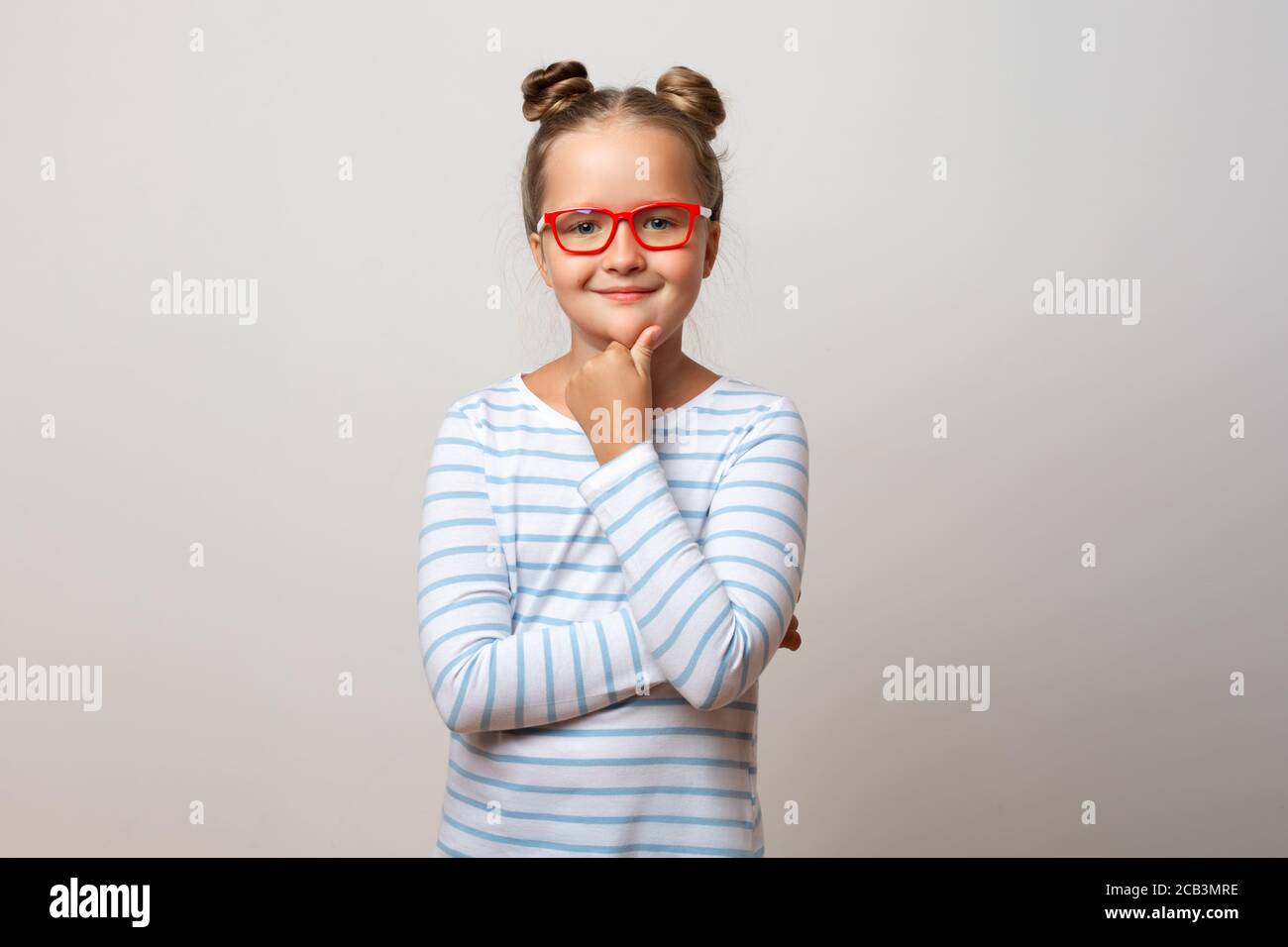 Portrait of a pensive thinking little schoolgirl girl in glasses on a white background. Child holding his chin with his hand. Stock Photo