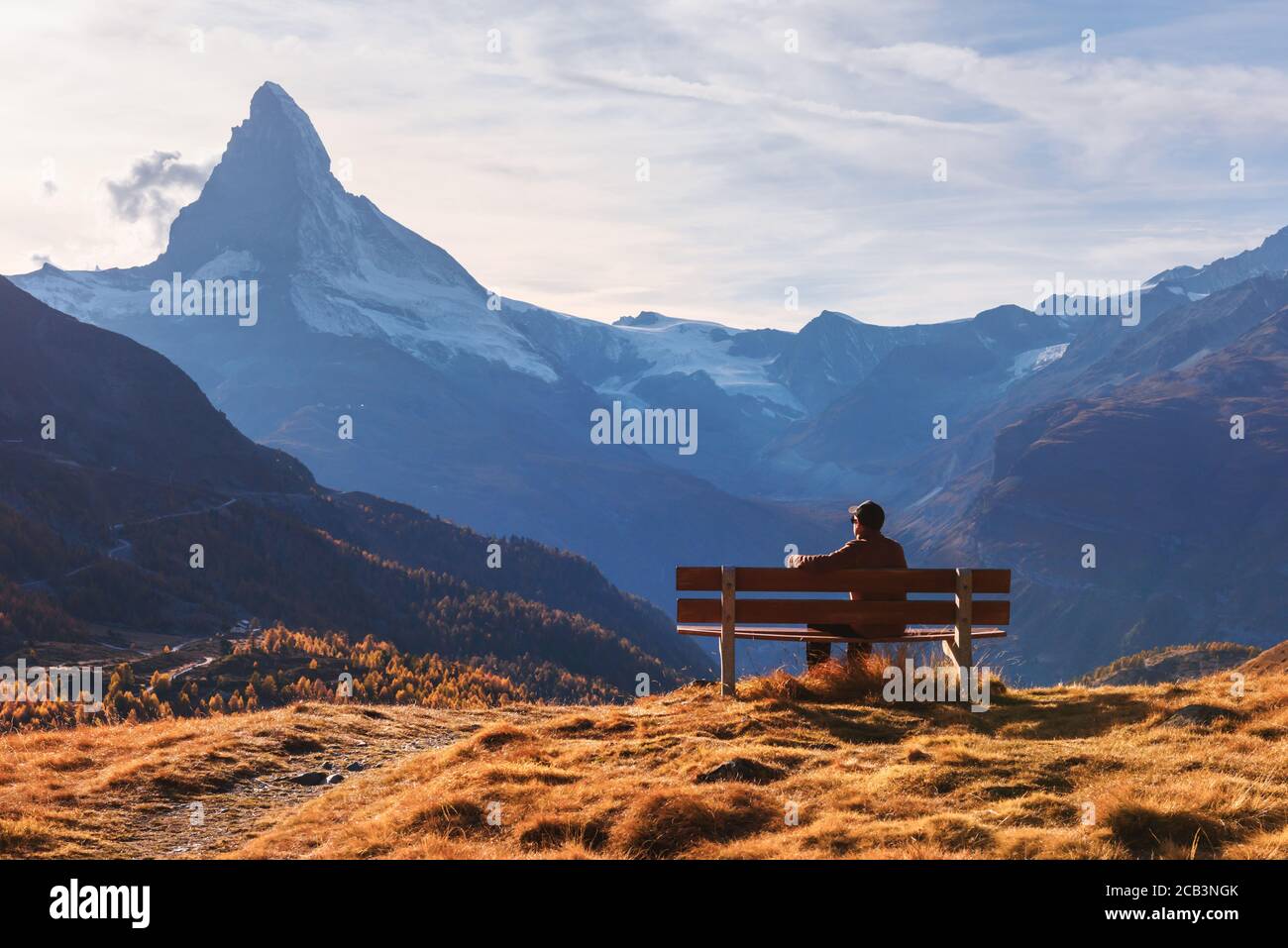 Picturesque view of Matterhorn peak and tourist sitting on wooden bench in Swiss Alps. Zermatt resort location, Switzerland. Landscape photography Stock Photo