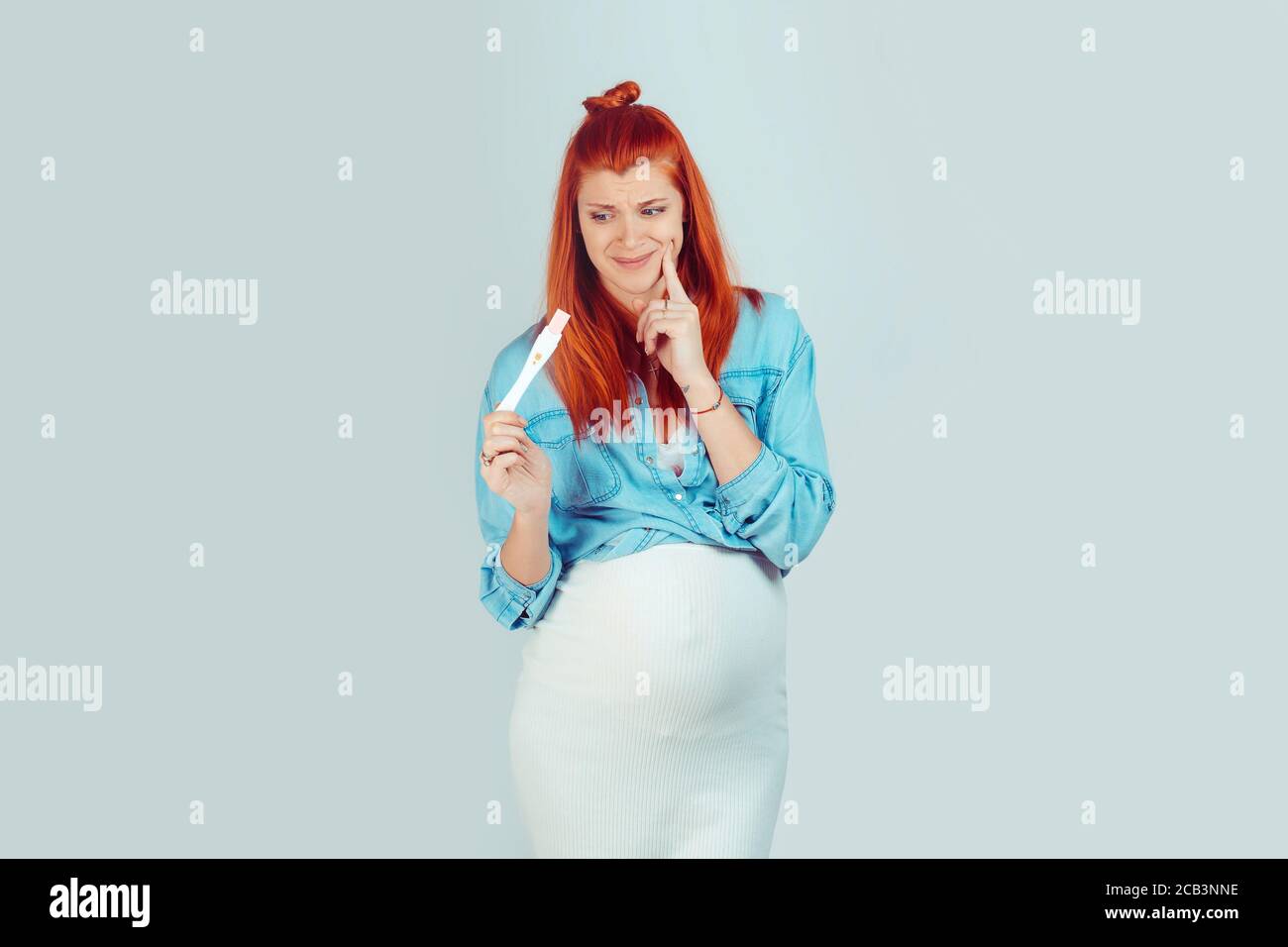 Young ginger girl with belly holding pregnancy test and looking confused and embarrassed