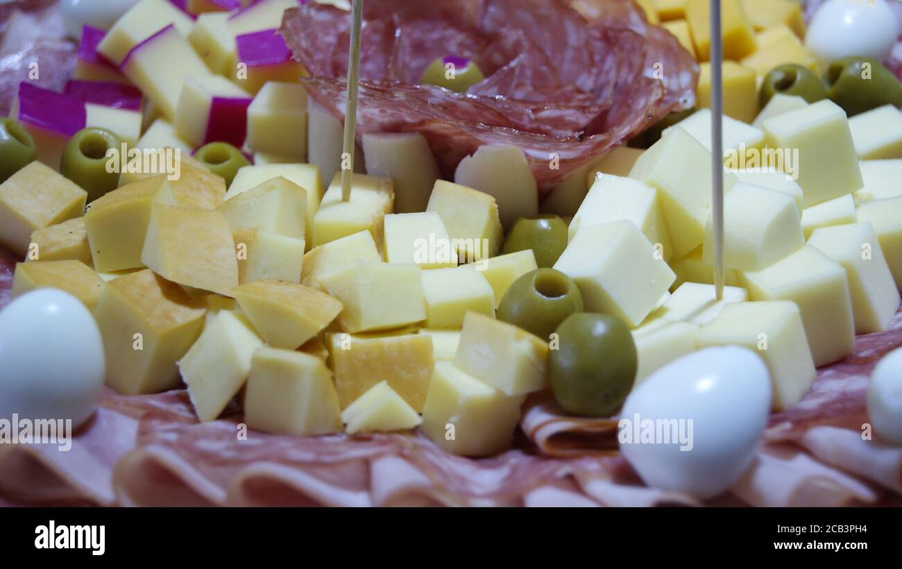 White dish decorated with salami, ham, quail eggs and green olives, on a background with a blue and white tablecloth, in photo zoom with detail Stock Photo