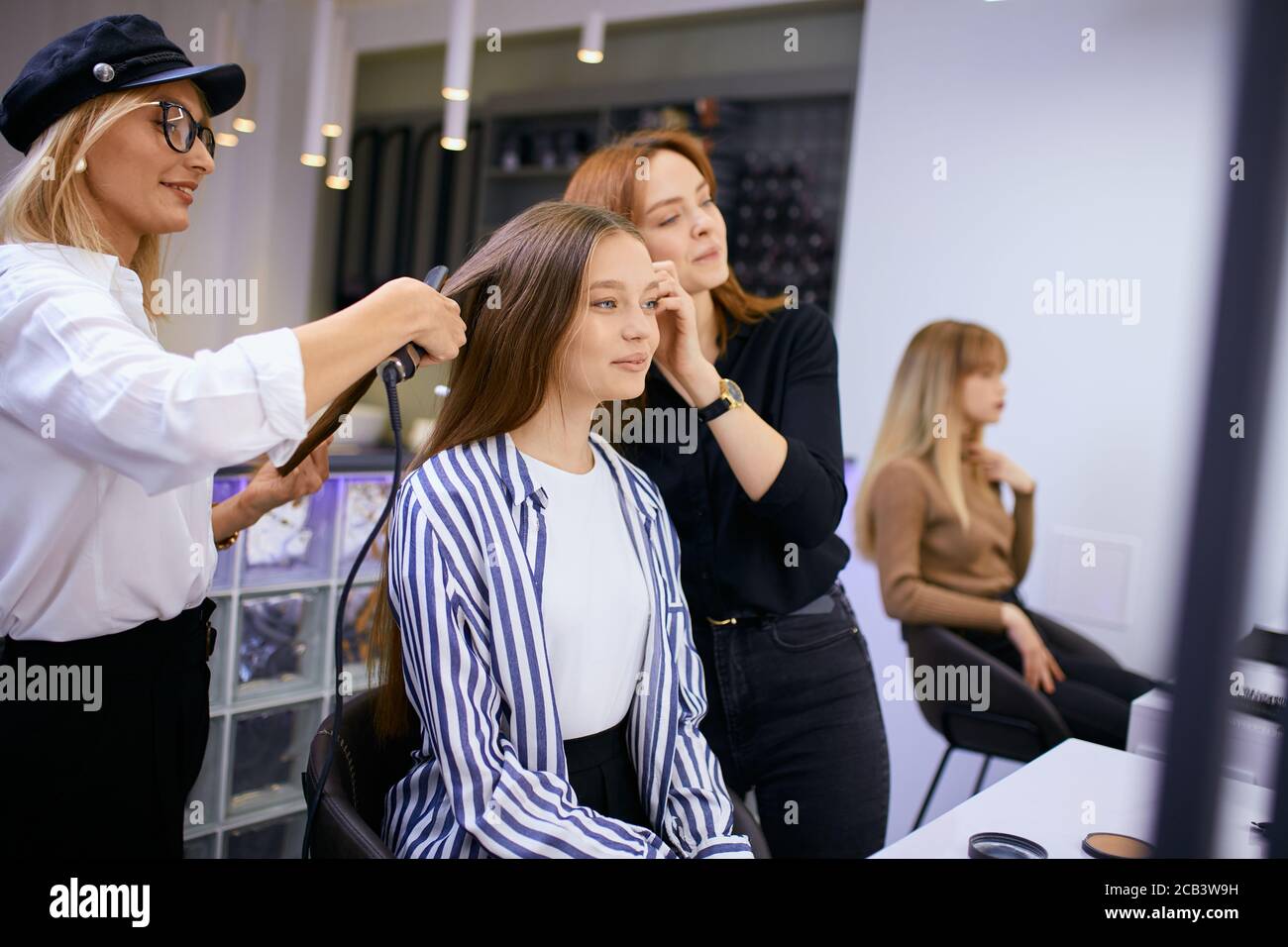 fashionable modern make-up artist doing makeup to young caucasian girl while hairdresser making hairdo in the background. Isolated in beauty saloon Stock Photo