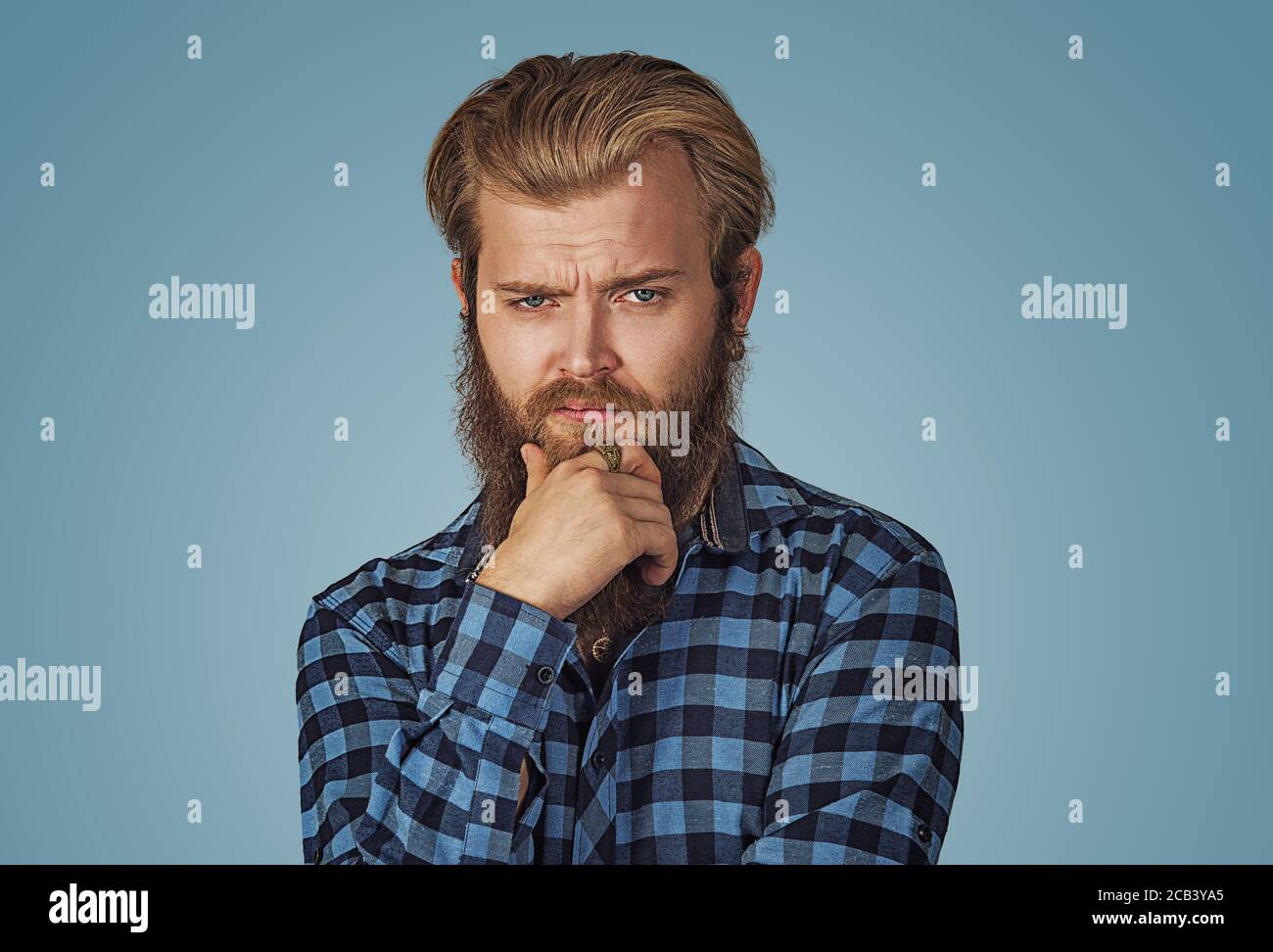 Frowning man thinking expressing doubts and concerns. Hipster male with beard in blue plaid checkered shirt  Isolated on blue studio Background. Negat Stock Photo