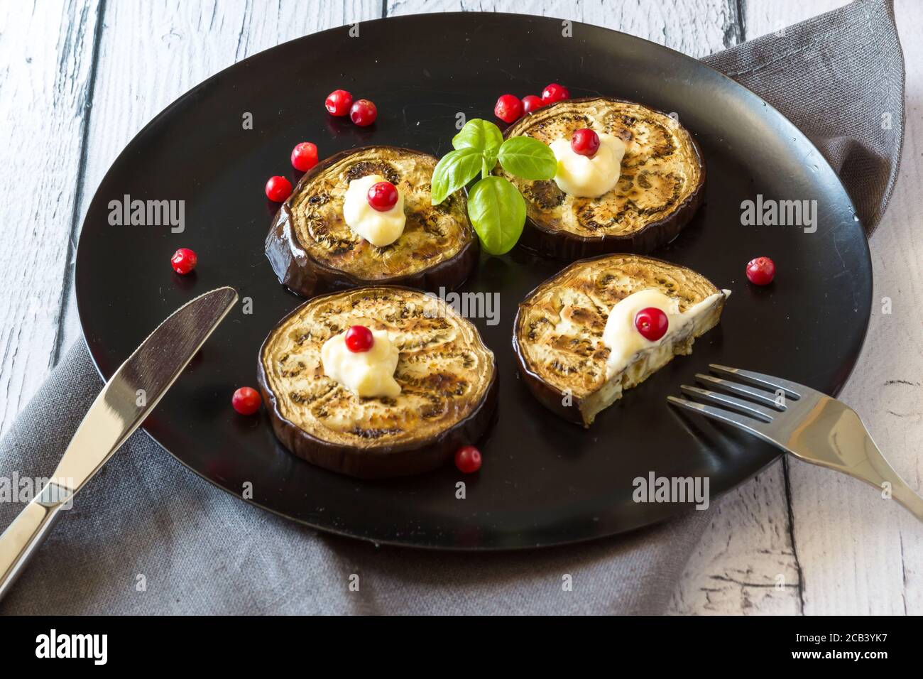Fried eggplant stuffed with cranberries, garnished with Basil leaves on a dark plate over wooden background. Top view. Stock Photo