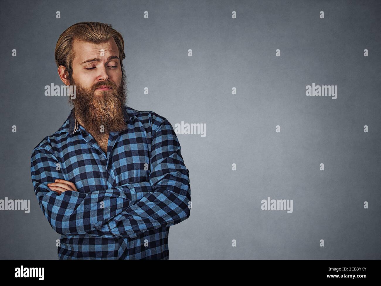 Suspicious skeptical man looking to the side to copyspace. Hipster male with beard in blue plaid checkered shirt  Isolated on gray grey studio Backgro Stock Photo