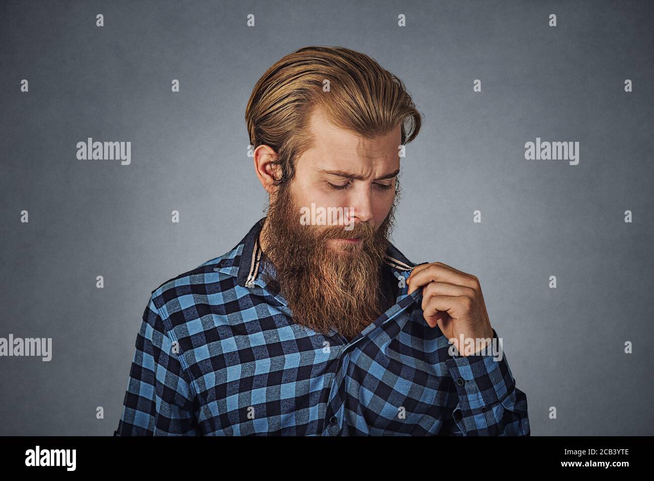 Man in awkward situation opening shirt to vent. Hipster male with beard in blue plaid checkered shirt  Isolated on gray grey studio Background. Negati Stock Photo