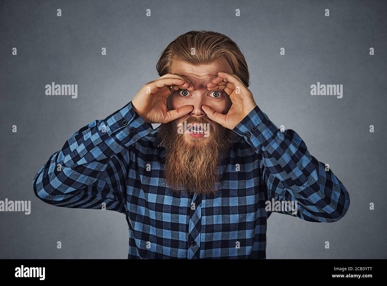 Closeup portrait young stunned curious man, peeking looking through fingers like binoculars searching something future forecast. Hipster male with bea Stock Photo