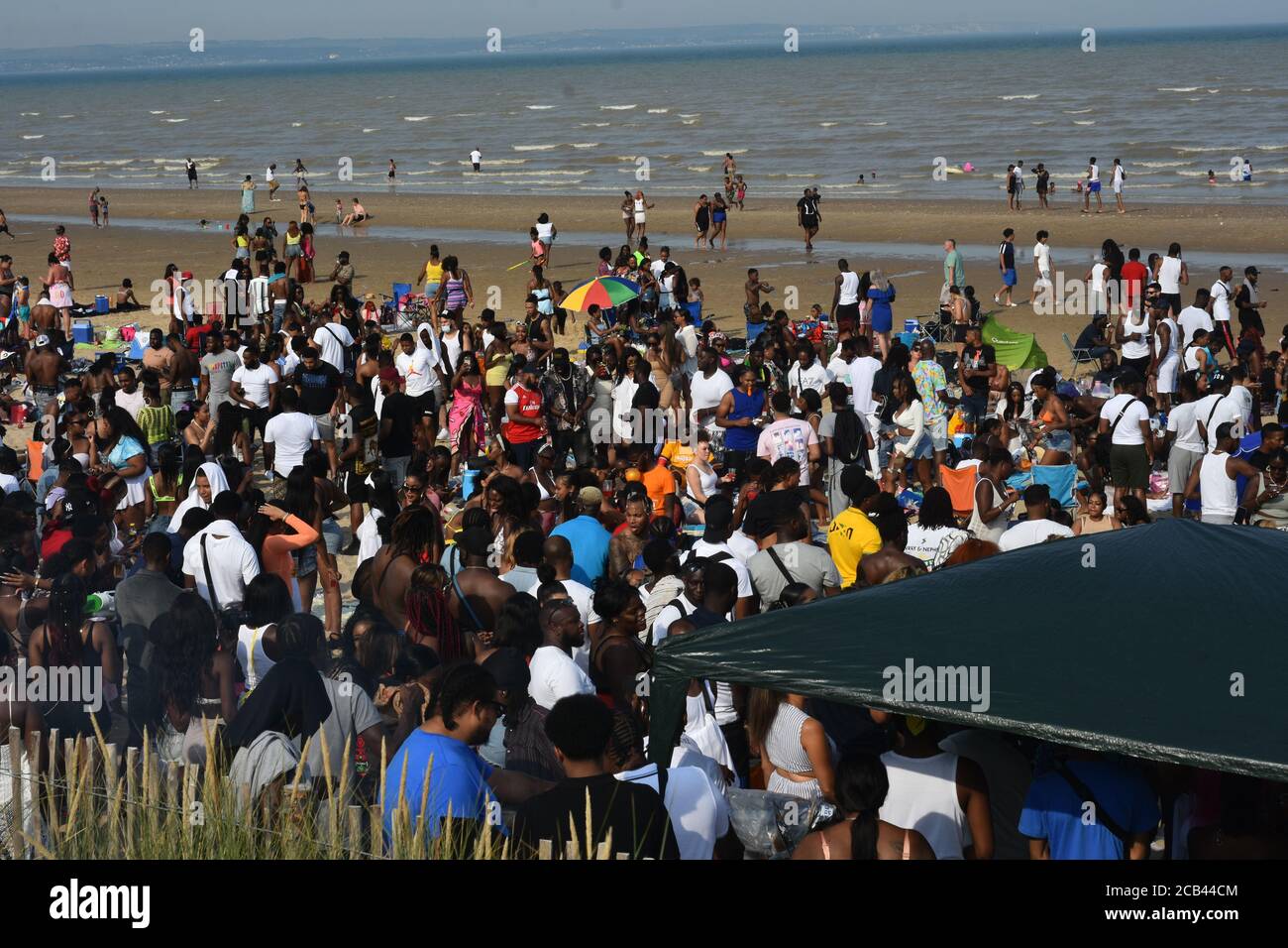 Hundreds descend upon the beach at Camber Sands to celebrate the anniversary of Jamaican independence which occurred back in 1962. Fears of a second spike of Covid 19 seemed to be in the backs of peoples minds as social distancing became difficult at times. Police presence observe the crowds at a safe distance while reminding people to keep a safe distance where possible. Event organisers encouraged social distancing throughout the day and asked everybody to be as safe and tidy as possible and also made a £750 donation to local litter picking to assist with litter Stock Photo