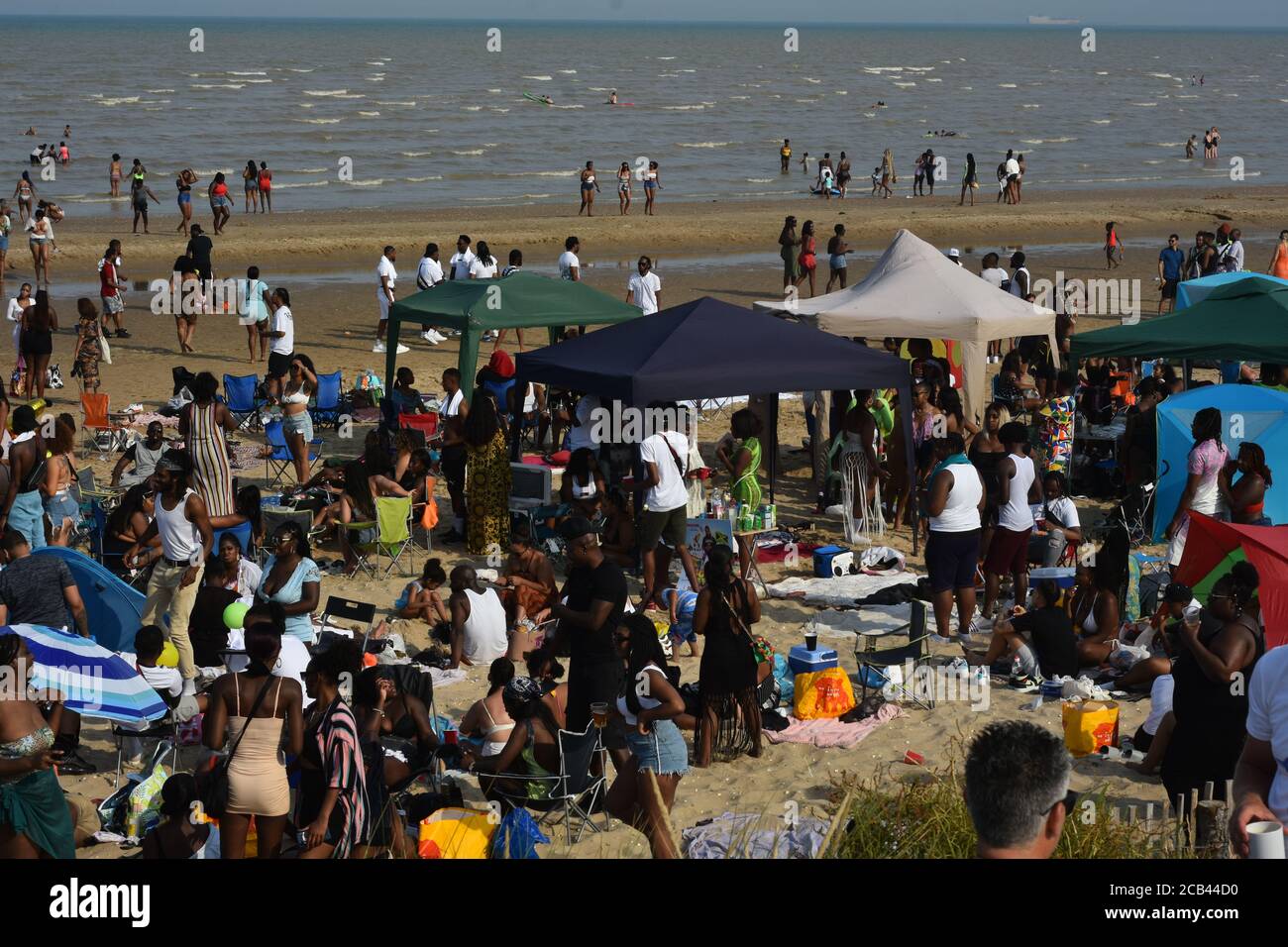 Hundreds descend upon the beach at Camber Sands to celebrate the anniversary of Jamaican independence which occurred back in 1962. Fears of a second spike of Covid 19 seemed to be in the backs of peoples minds as social distancing became difficult at times. Police presence observe the crowds at a safe distance while reminding people to keep a safe distance where possible. Event organisers encouraged social distancing throughout the day and asked everybody to be as safe and tidy as possible and also made a £750 donation to local litter picking to assist with litter Stock Photo