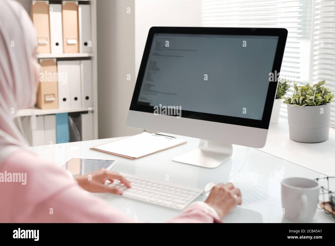 Over shoulder view of Muslim programmer sitting at office table and coding information for website using computer Stock Photo