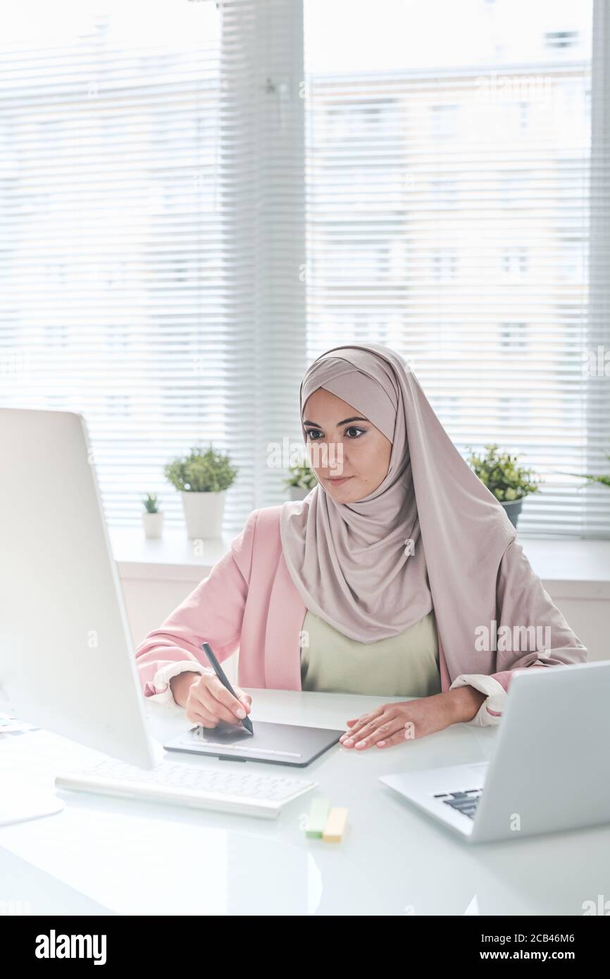 Busy young Muslim graphic designer in beautiful hijab sitting at desk and  using digitizer for work Stock Photo - Alamy