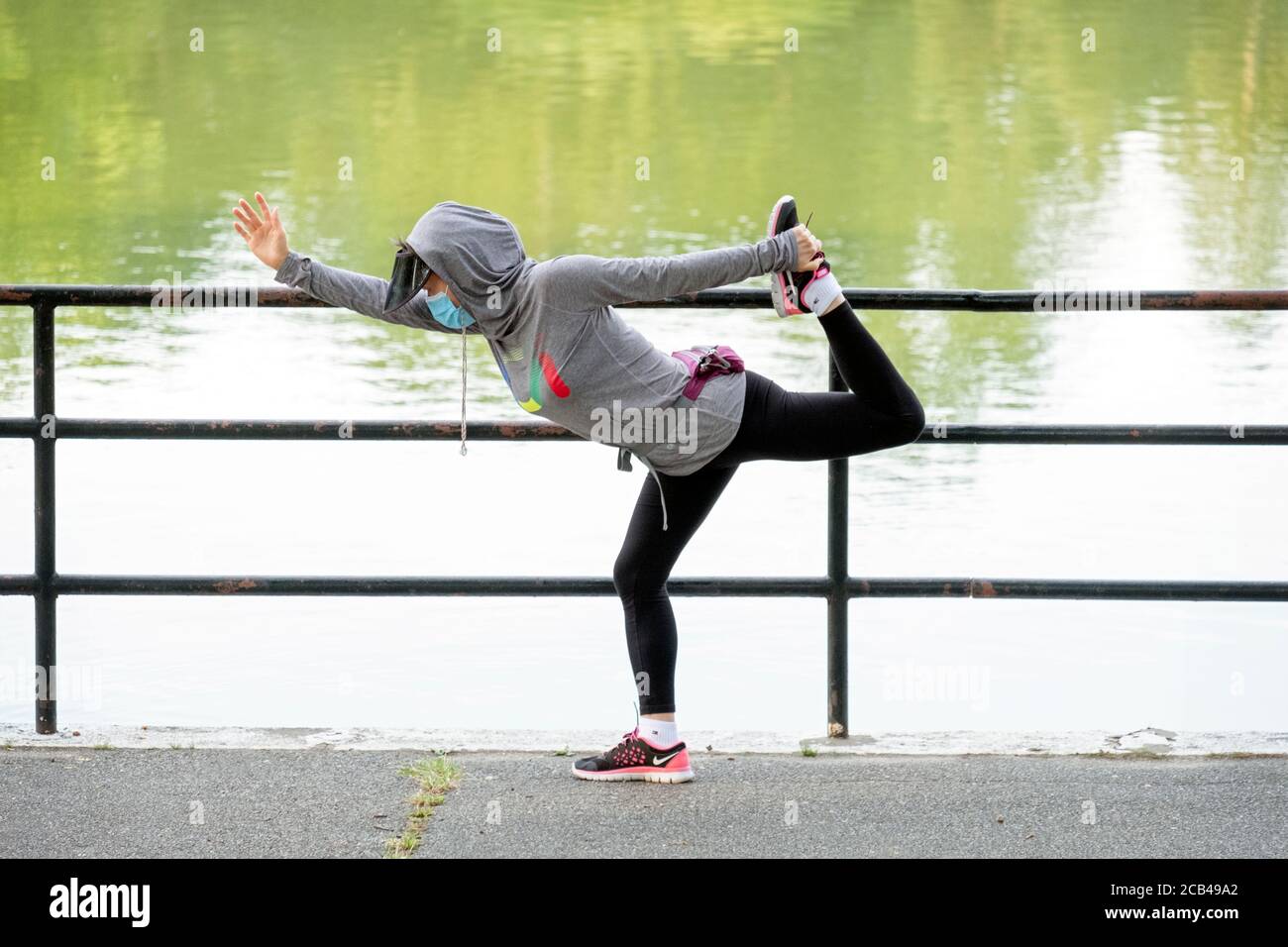A nimble Asian American woman wearing a mask stretches before exercising. In Kissena Park, Flushing, New York City. Stock Photo