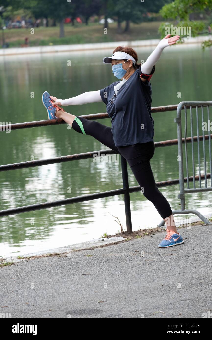 An Asian American woman wearing a surgical mask stretches before exercising. In Kissena Park, Flushing, New York City. Stock Photo