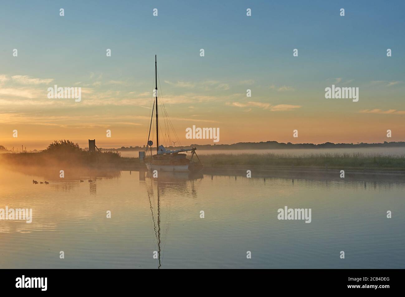 Potter Heigham, Norfolk Broads and a sailing boat moored on the River Thurne during a misty summer sunrise. Stock Photo