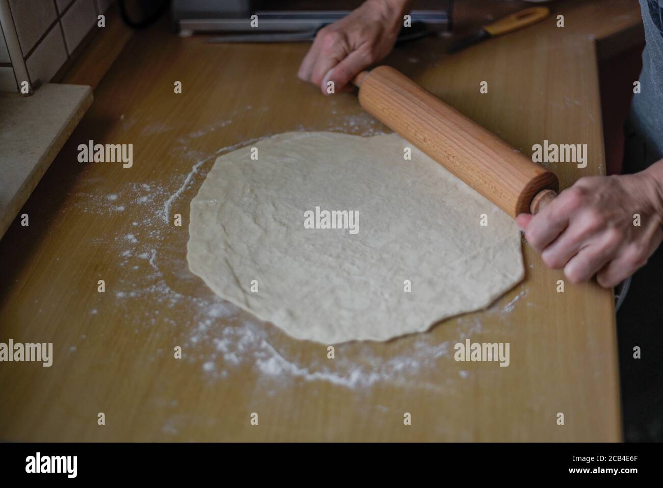 Selective focus shot of a female roll out the dough with a wooden rolling pin in the kitchen Stock Photo