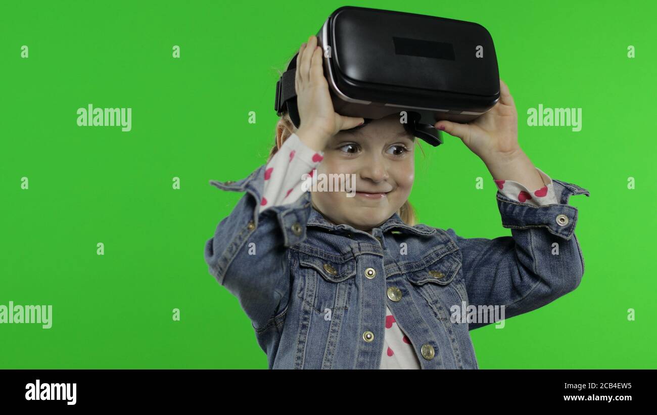 Child teen girl using VR app headset helmet to play simulation game,  drawing. Watching virtual reality 3d 360 video. Isolated on chroma key  green background in studio. Kid in VR goggles looking