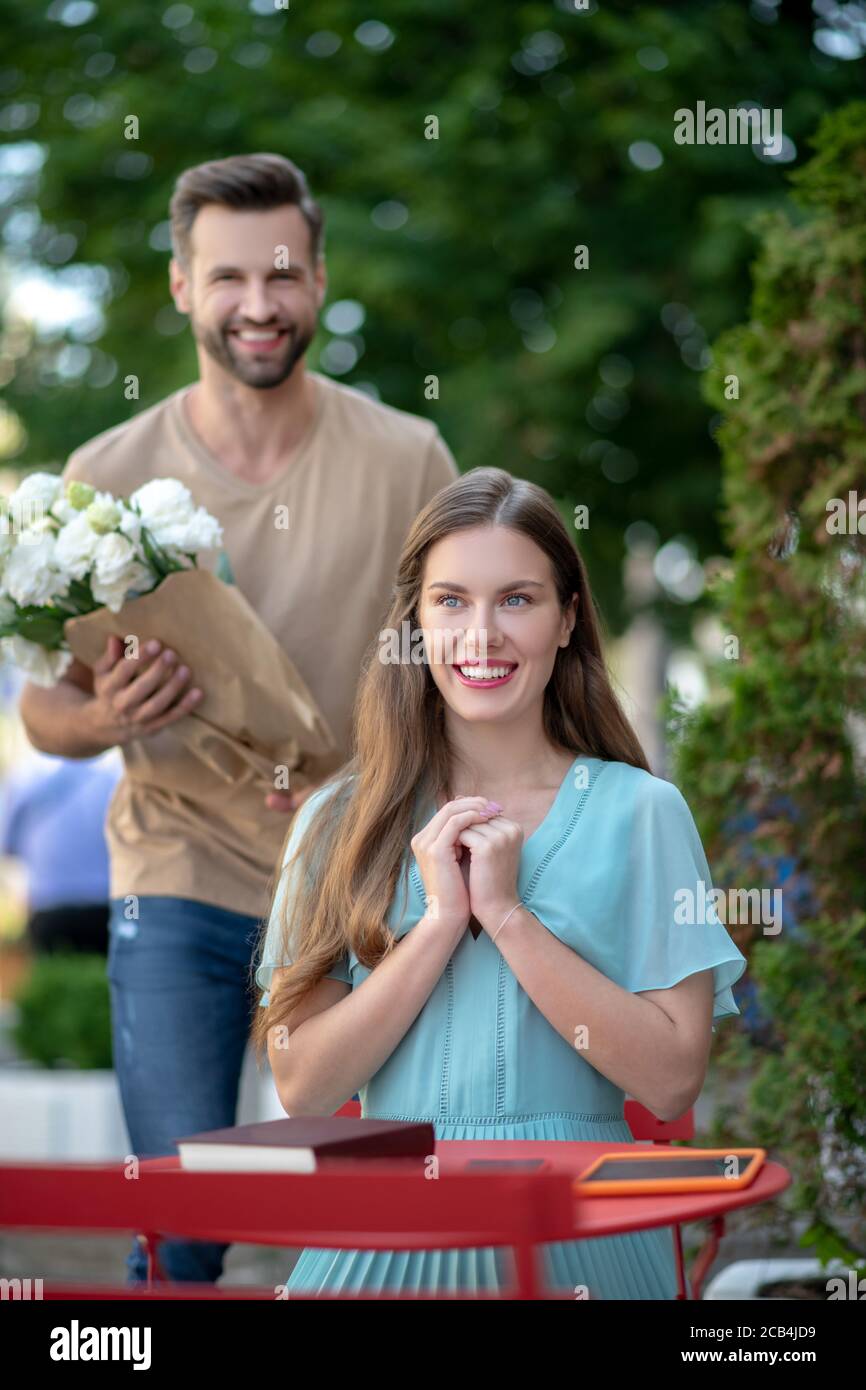 Young female sitting in the cafe, bearded male coming to her with flowers Stock Photo