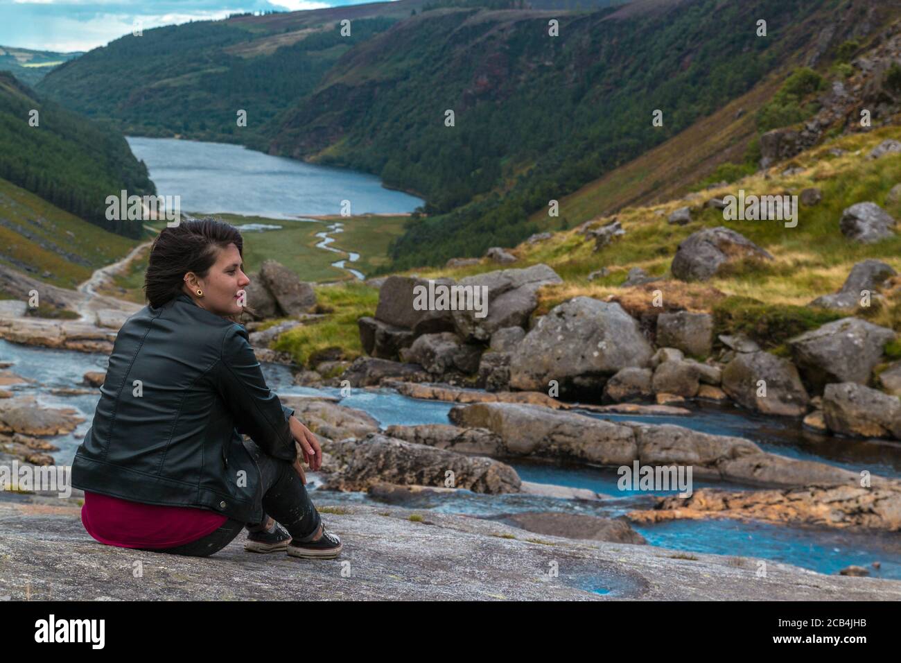 Woman sitting on the hill at the Glendalough Valley. Wicklow Mountains, Ireland. Stock Photo