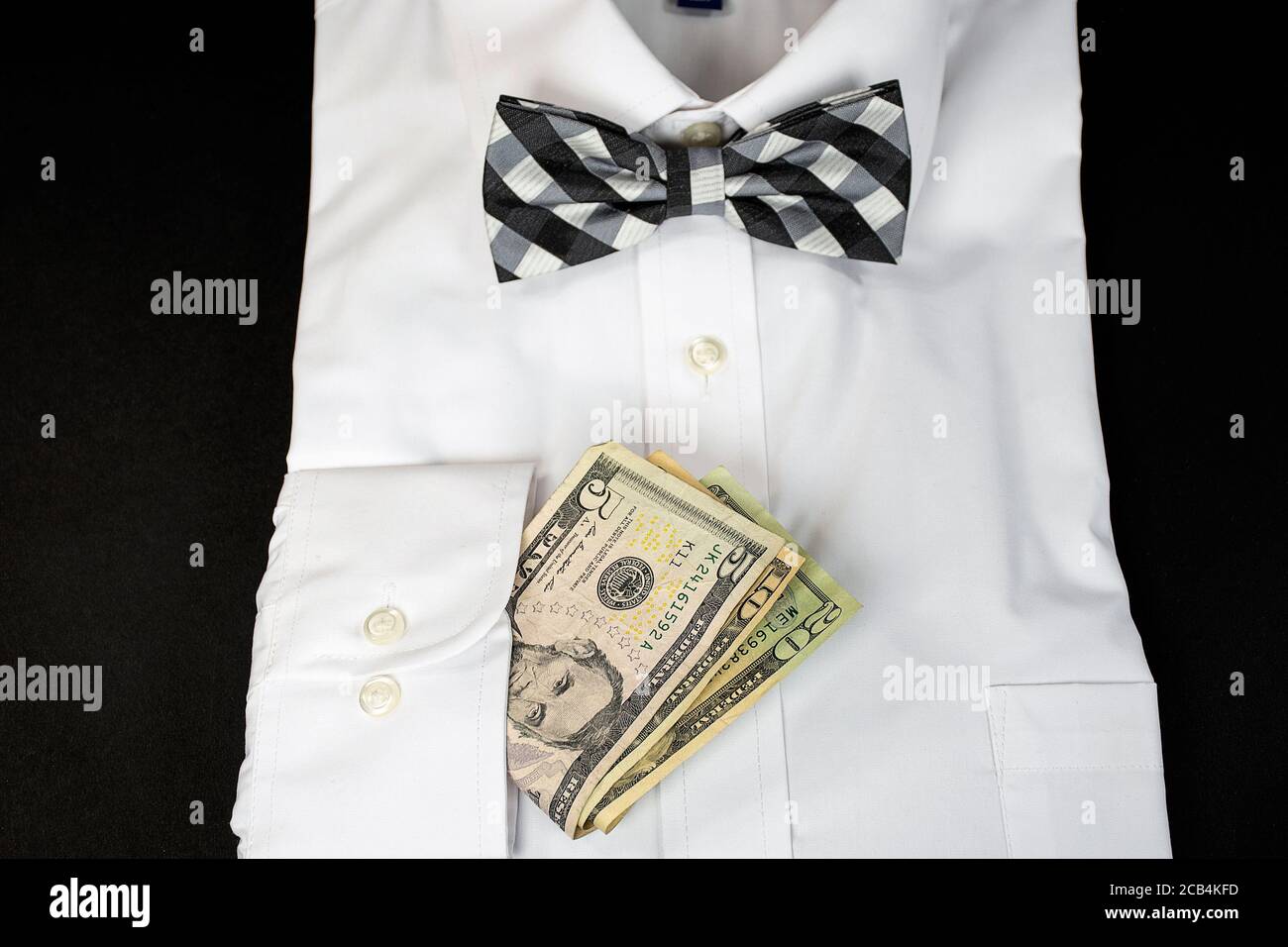 man's white dress shirt with black and white checkered bow tie and American money in sleeve cuff Stock Photo