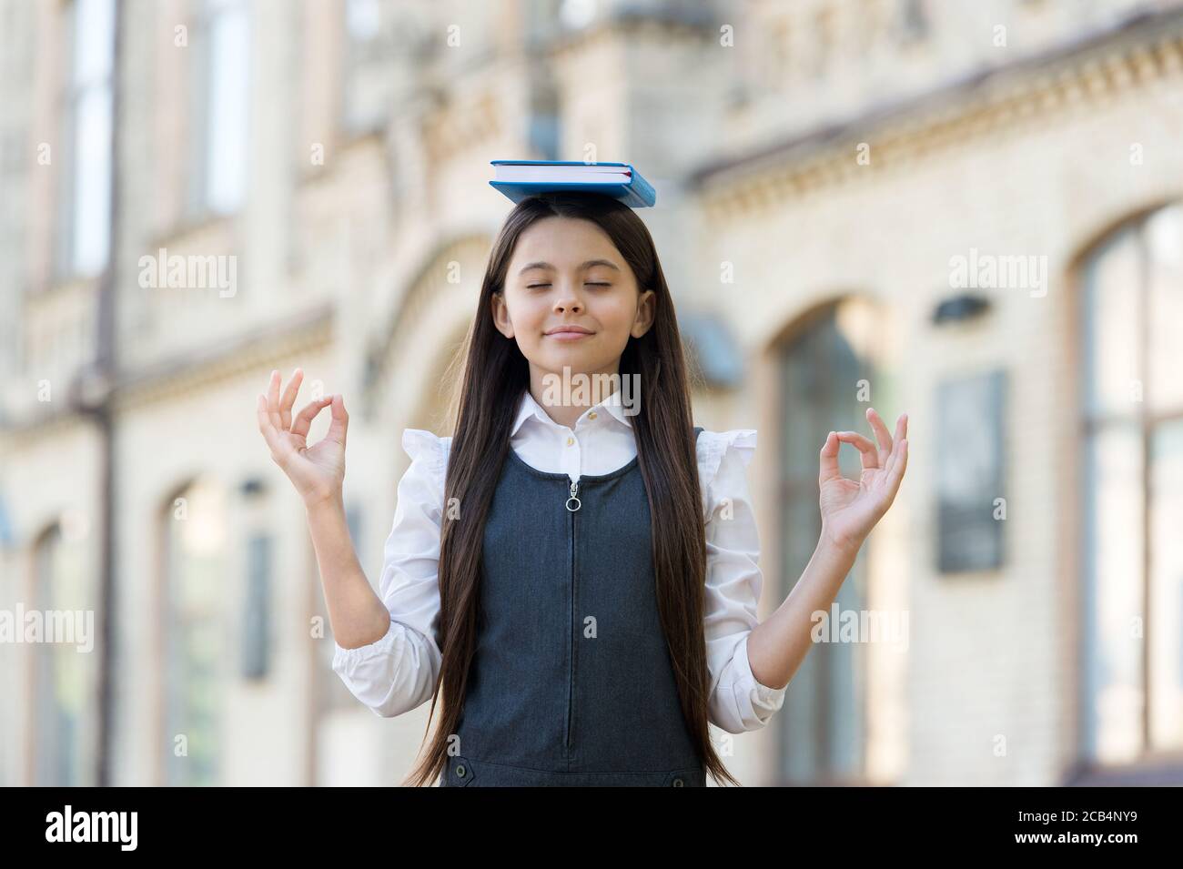 Calm the mind. Little child do meditation outdoors. Small girl do mudra hands holding book on head. Meditation for mental balance. Meditation course for beginner. School and education. Best therapy. Stock Photo