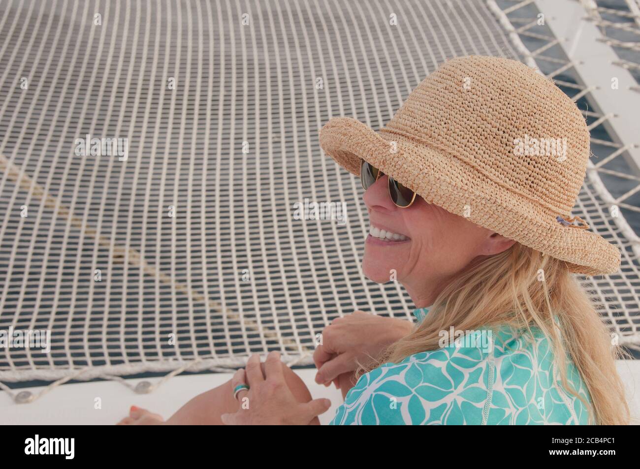 Happy outside. 60-year old active senior mature woman in straw hat on a boat smiling with big smile and white teeth. Happy retirement. Model release. Stock Photo