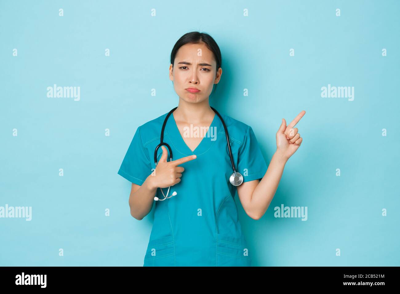 Covid-19, social distancing and coronavirus pandemic concept. Complaining disappointed asian female doctor, intern or nurse in scrubs sulking upset Stock Photo