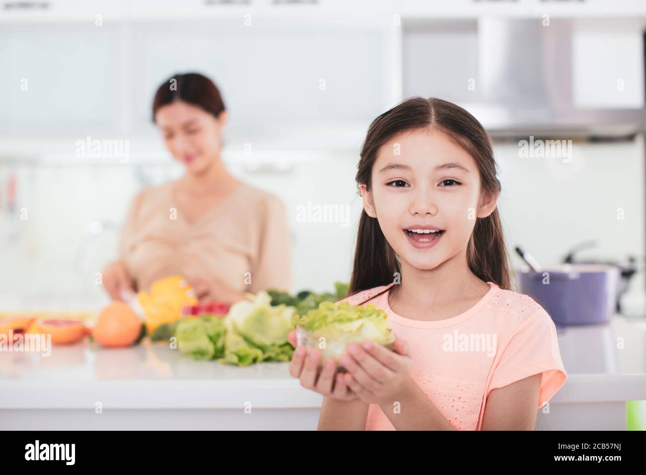 mother working at kitchen and daughter showing health food Stock Photo