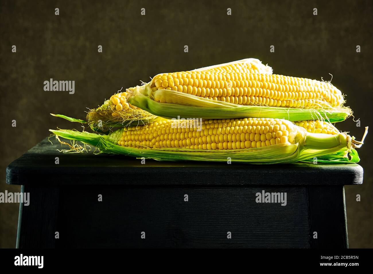 Cobs of ripe raw corn on a dark wooden table. healthy food, fresh raw corn cobs, rustic style Stock Photo