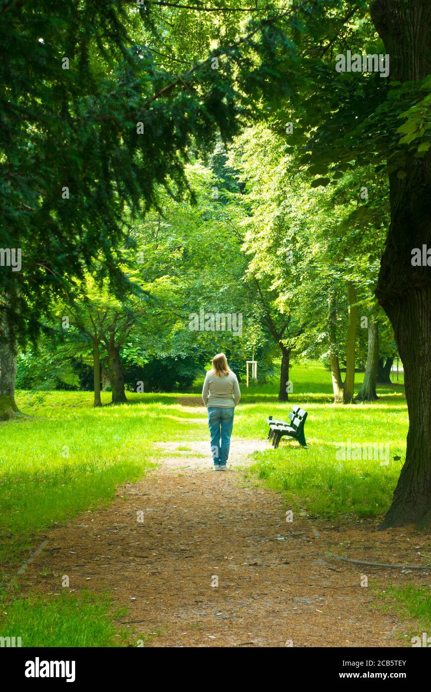 blonde woman standing in a park surrounded by trees and silence, communion with nature and soul searching concept Stock Photo