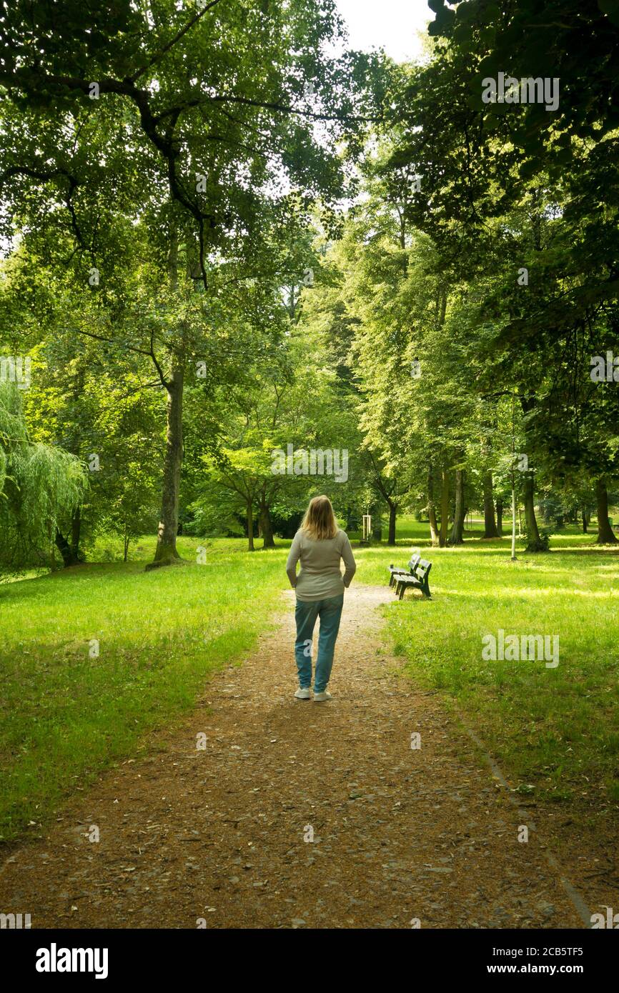 blonde woman standing in a park surrounded by trees and silence ...