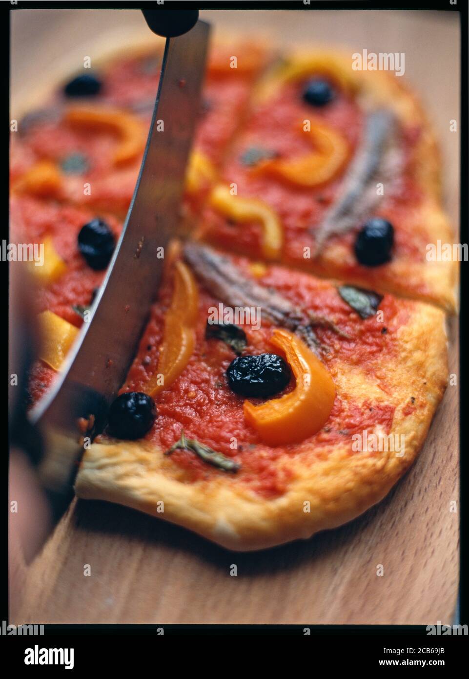 Cutting a homebaked tomato based pizza topped with olives, peppers,basil and anchovies topping Stock Photo