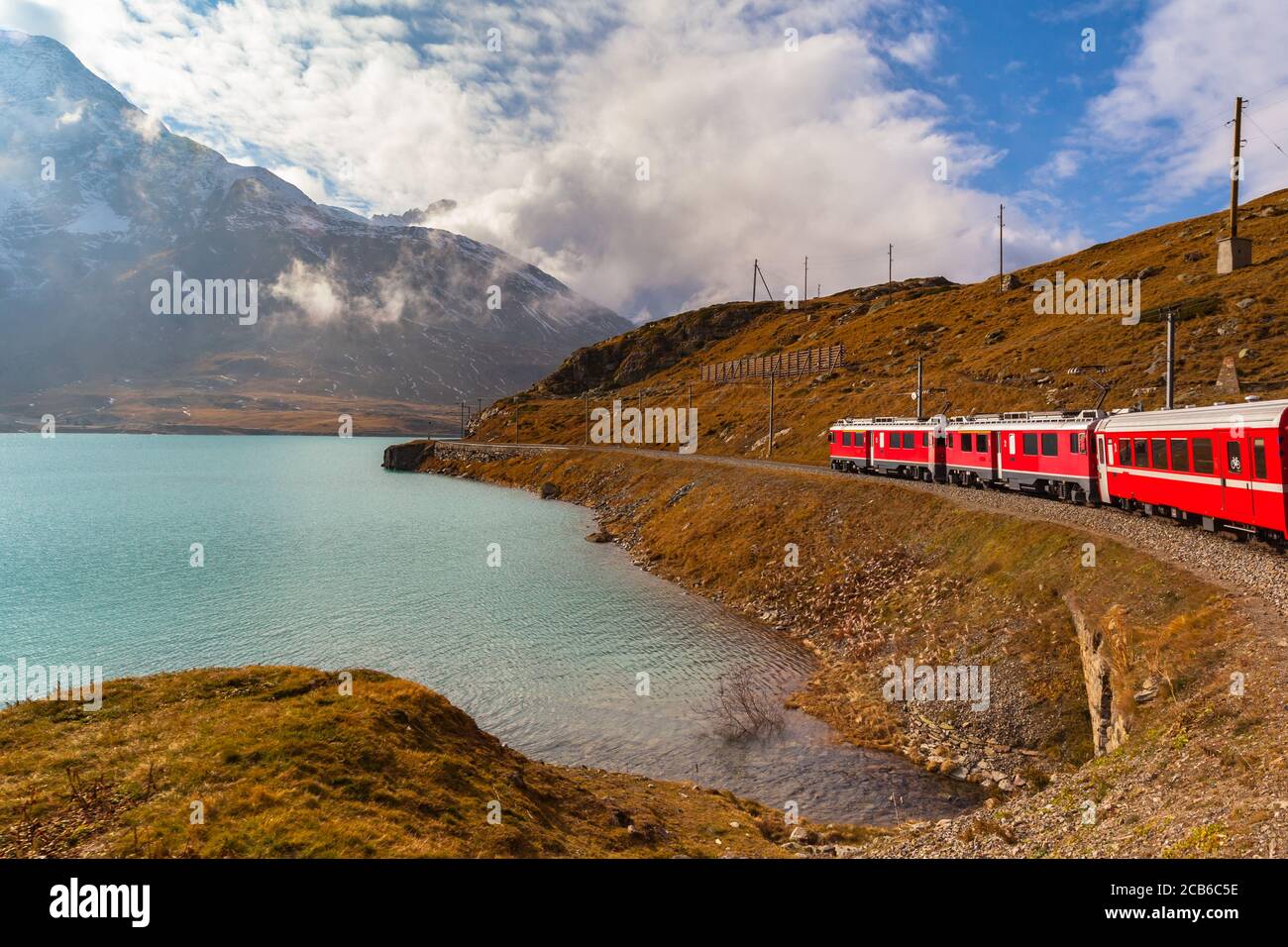 Beautiful view of  Rhaetian railway red train running on the lake side of Lago Bianco in autumn with blue sky cloud, on sightseeing railway line Berni Stock Photo