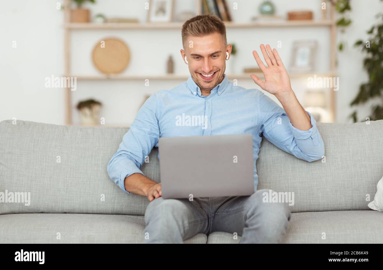 Happy guy using laptop for video call and waving Stock Photo - Alamy