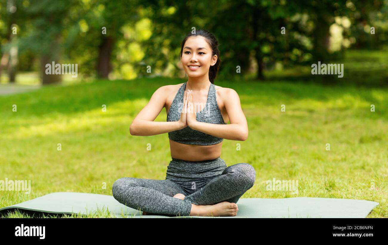 Calm Asian girl meditating in lotus pose during her yoga class outdoors Stock Photo