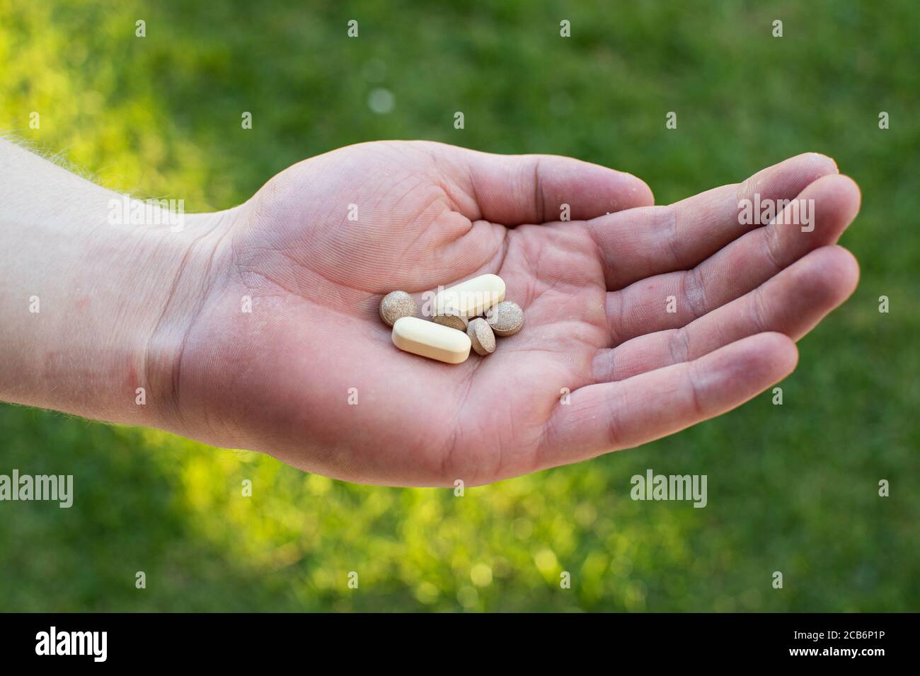 Brown and yellow Multi vitamin health pills cupped in a hand with a green natural background behind promoting health and well being Stock Photo