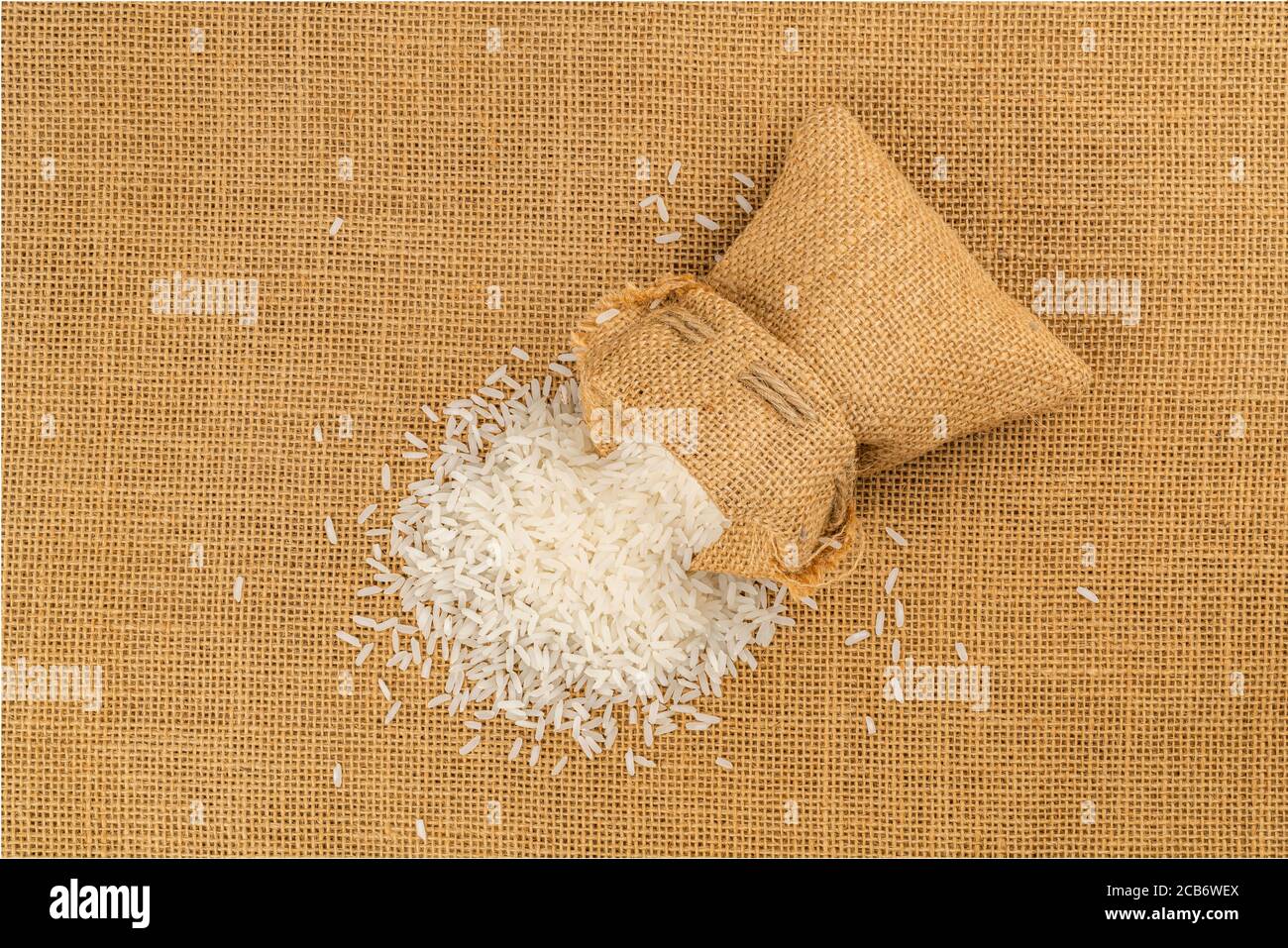Top view of jasmine rice flow out from a sack on the floor covered with sackcloth. Stock Photo