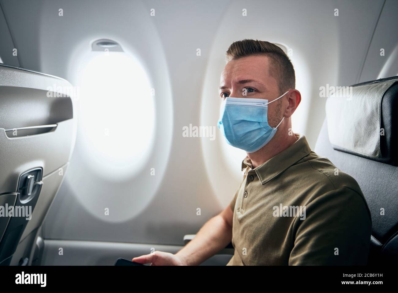 Man wearing face mask inside airplane during flight. Themes new normal, coronavirus and personal protection. Stock Photo
