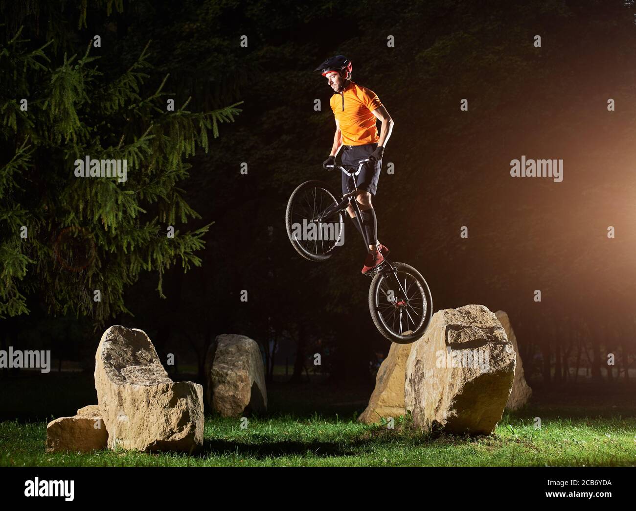 Side view of fearless guy doing trick while standing on a bike. Cyclist holding handlebar in hand and doing stunt on stone. Concept of motion. Stock Photo