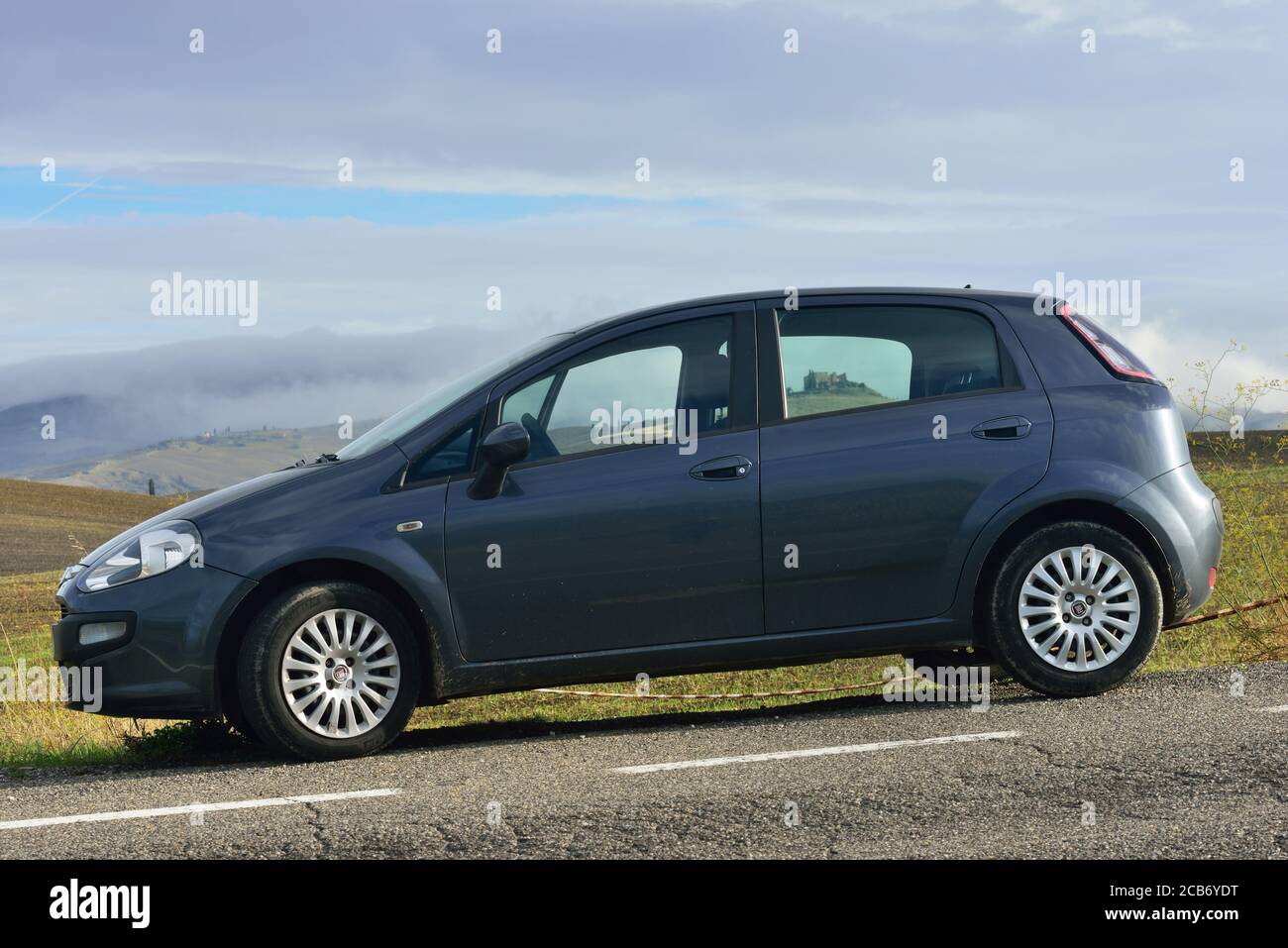 Pienza, Italy - October 13, 2012: Fiat Punto Evo car parked in front of wonderful landscape with hills with autumns grain fields and old castle seen t Stock Photo