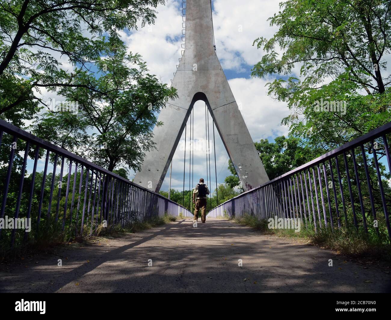 A tourist with a backpack crosses the metal bridge in summer. Stock Photo