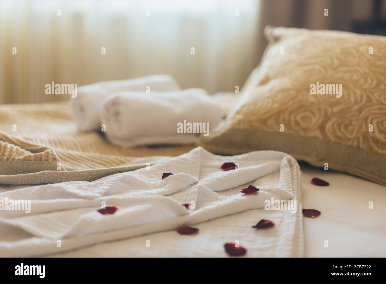 Luxury wellness and spa hotel room arranged for romantic weekend. Honeymoon suite bedroom decorated with rose petals on bed sheets and clean towels. R Stock Photo