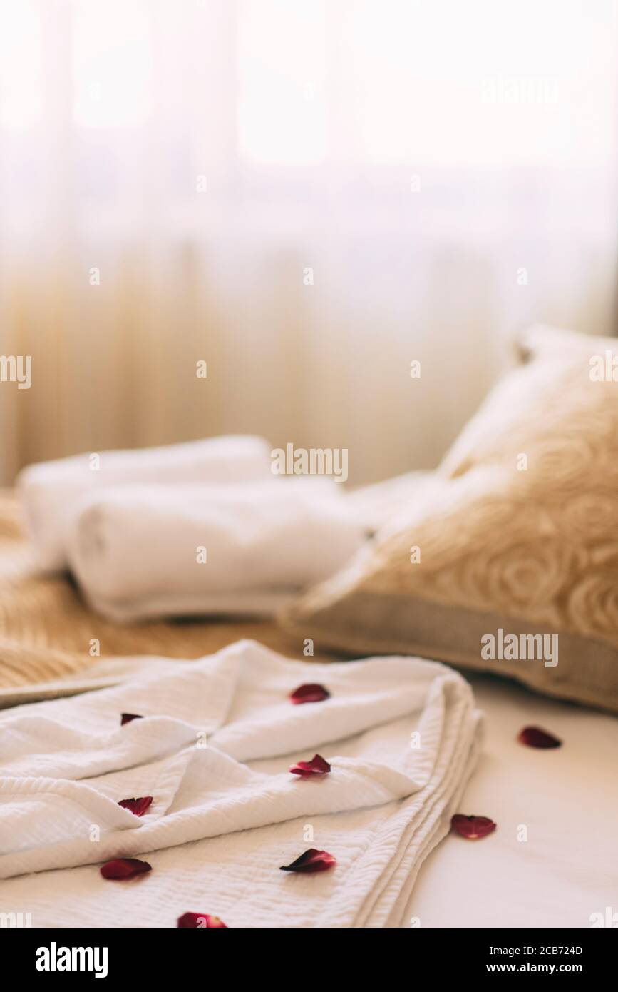 Luxury wellness and spa hotel room arranged for romantic weekend. Honeymoon suite bedroom decorated with rose petals on bed sheets and clean towels. R Stock Photo